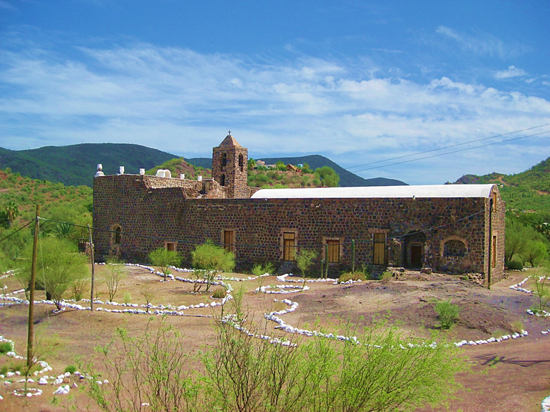 A large stone building with a mountain in the background Description automatically generated